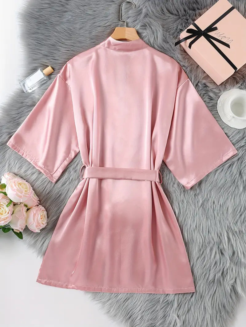 Customisable Pink spa robe on a hanger with a gift box and flowers on a grey surface, buy spa products, add on to pa packages